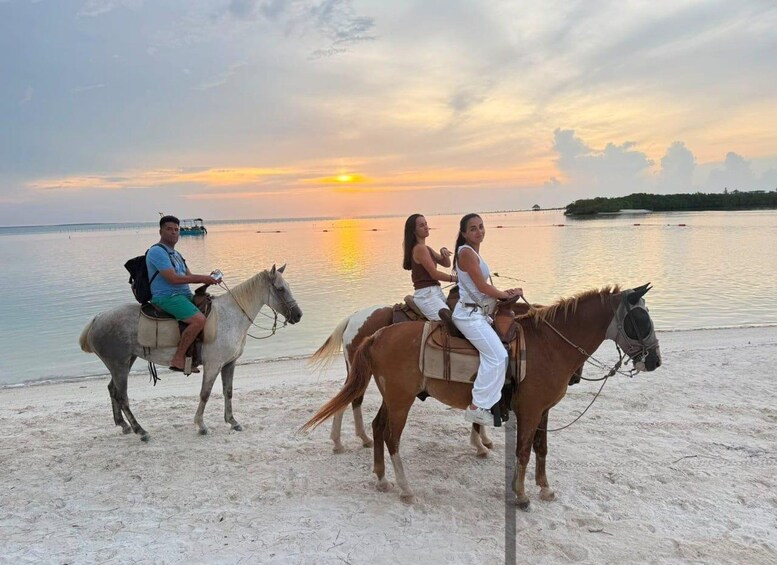 Three people riding horses on a beach at sunset. 5