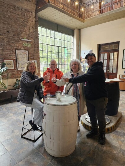 A group of people toasting with wine glasses around a barrel in a rustic interior with brick walls and large windows. 2