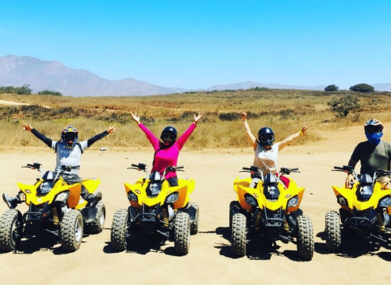 Four people on quad bikes in a desert landscape with mountains in the background. 5