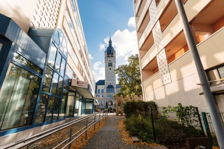 A cobblestone path leading to a tower with a clock, surrounded by modern buildings and a tree. 3
