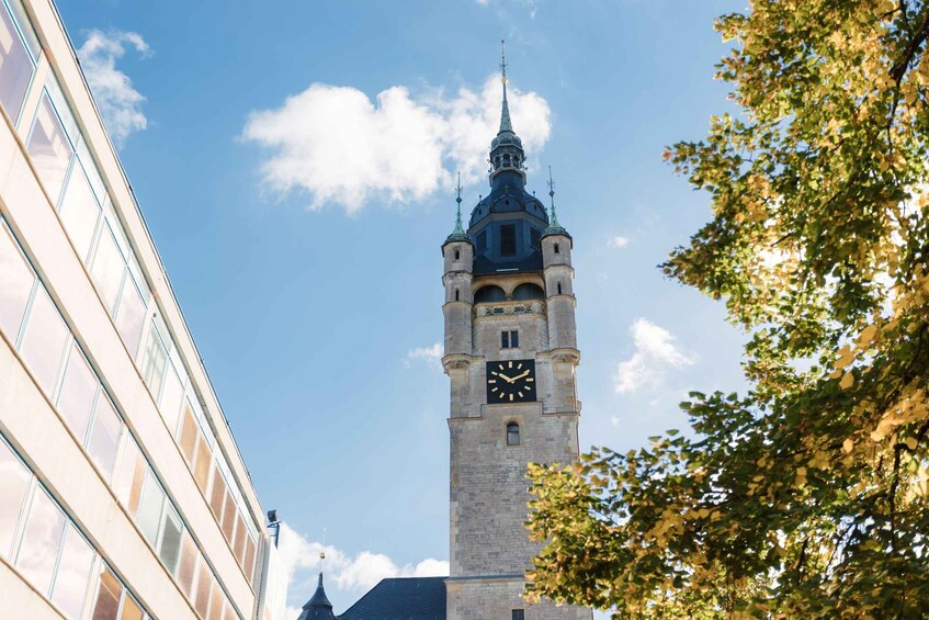 A clock tower with a spire, surrounded by trees and a modern building. 5