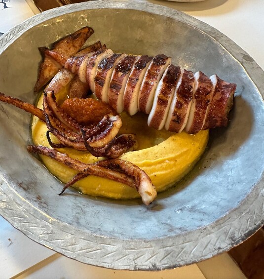 A roasted pork loin with crispy skin, served on a bed of mashed potatoes in a metal bowl. 2