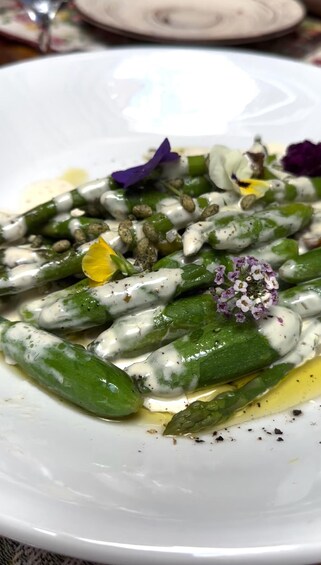 A plate of asparagus with a creamy sauce, garnished with flowers and herbs. 3