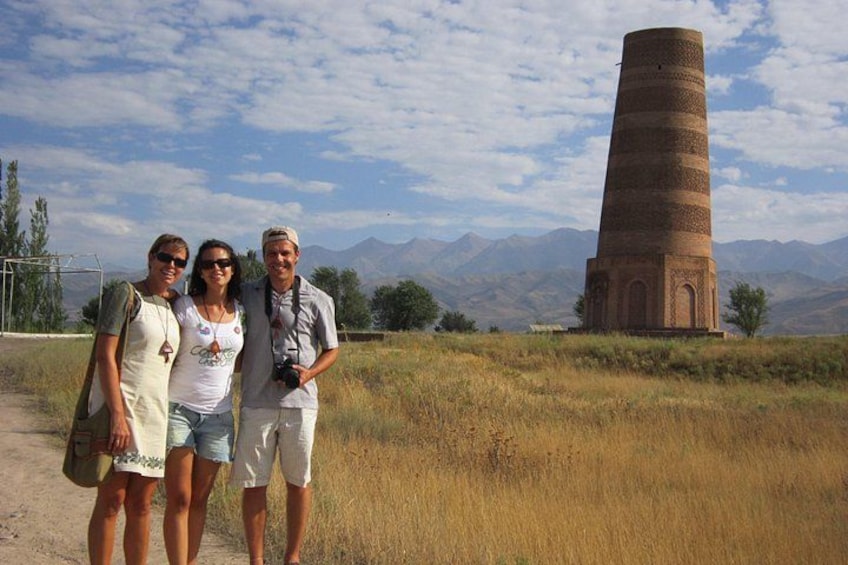 Three people standing in front of a tall brick tower with mountains in the background. 5