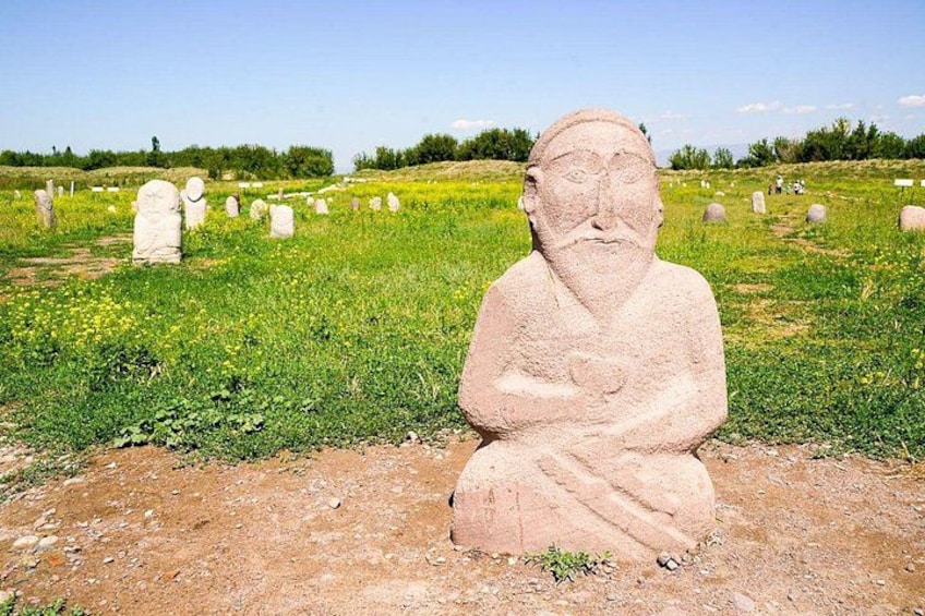 A stone statue in a grassy field with multiple headstones in the background. 2
