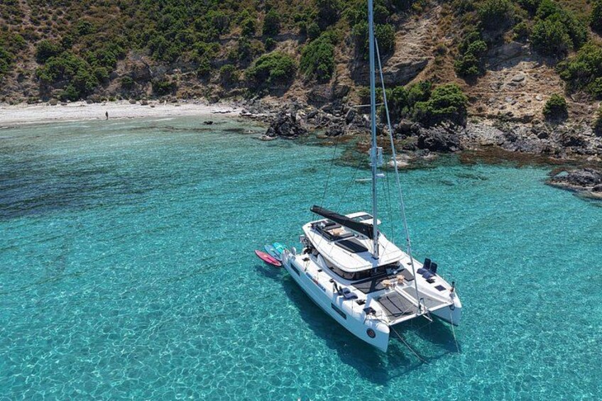 A sailboat anchored in clear turquoise waters with a rocky coastline in the background. 2