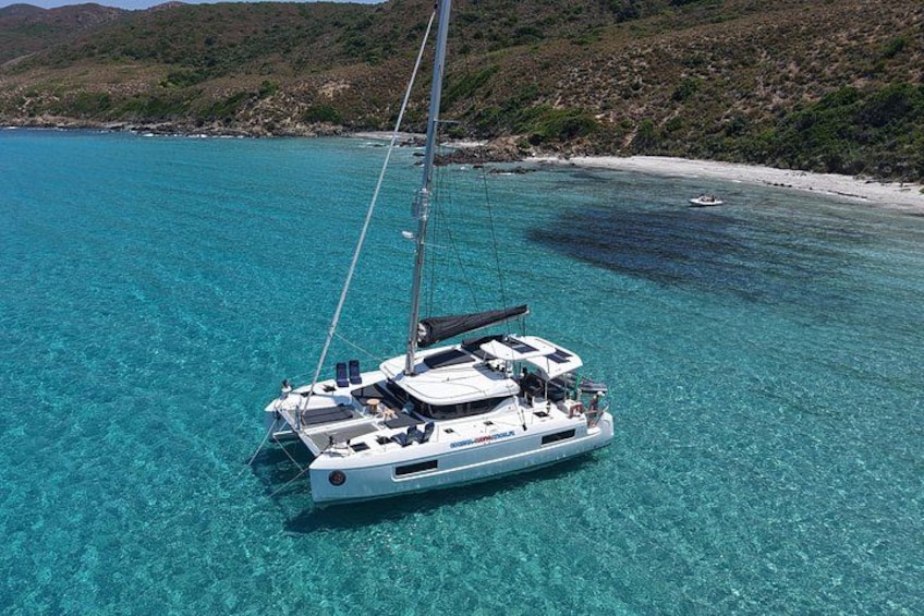 A sailboat on clear turquoise water with a beach and hills in the background. 3