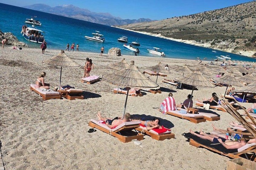 A beach with sun loungers, umbrellas, and boats in the water. 3