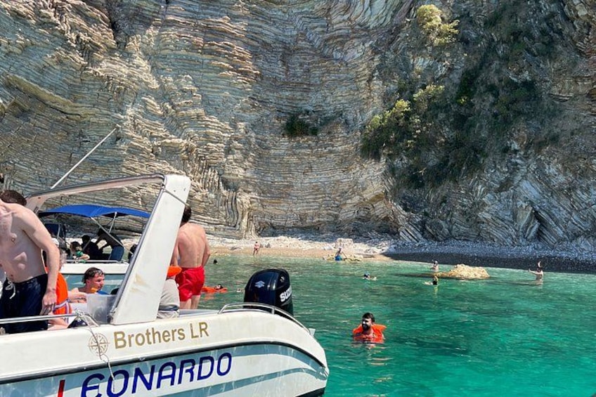 A boat named 'Leonardo' with people swimming in the water and cliffs in the background. 2