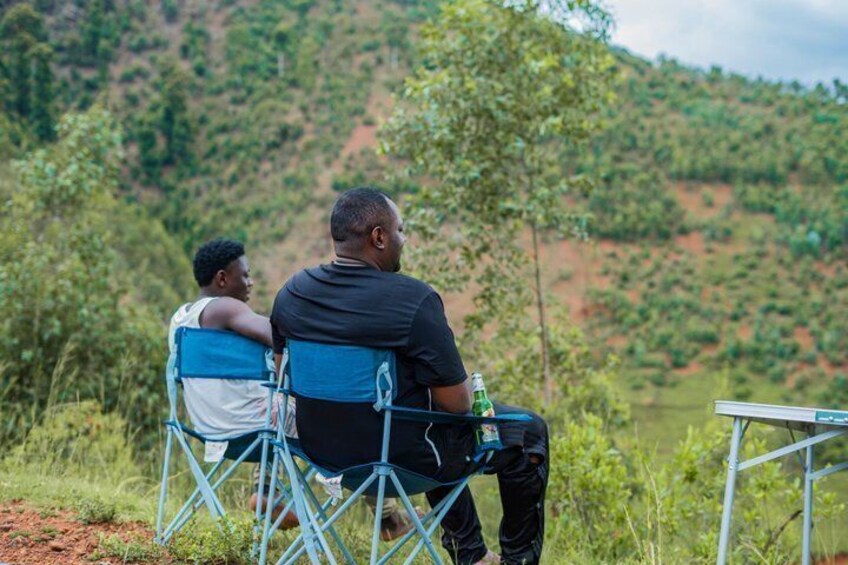 Two people sitting on blue folding chairs outdoors with a green bottle on the table. 5