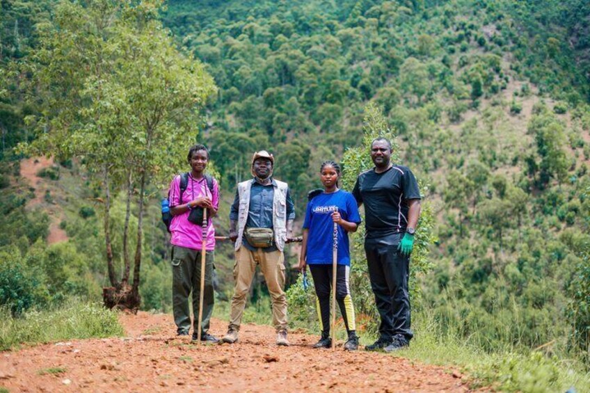 Four people standing on a dirt path with a forested hillside in the background. 2