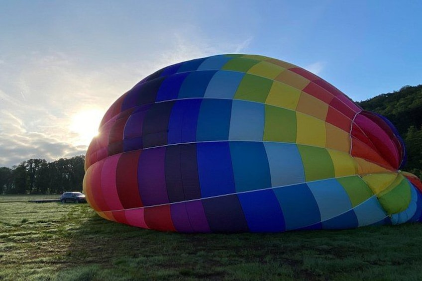 A large, colorful hot air balloon parked on grass with a clear sky and trees in the background. 4