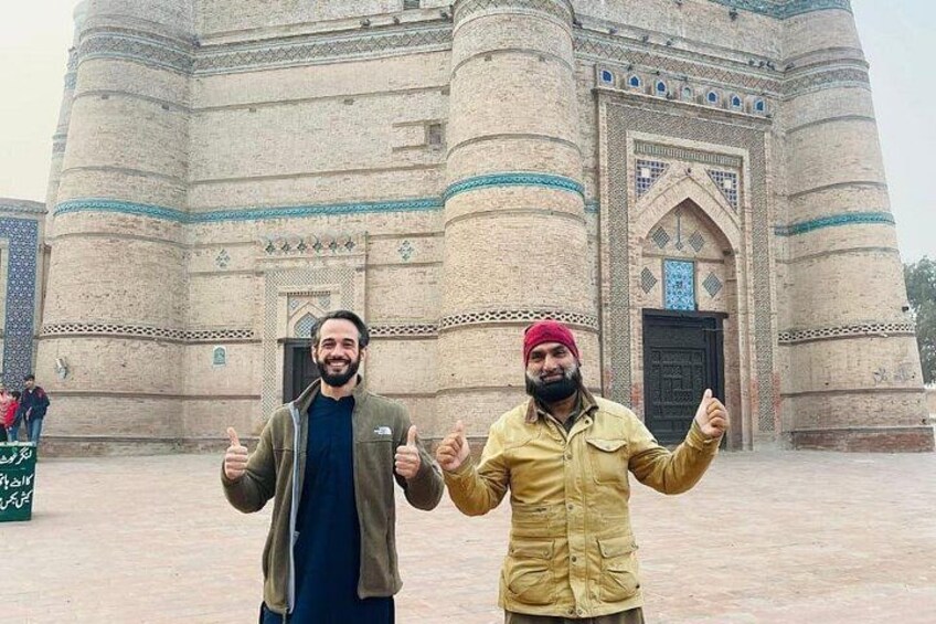 Two men giving thumbs up in front of a large, historic building with intricate designs. 2