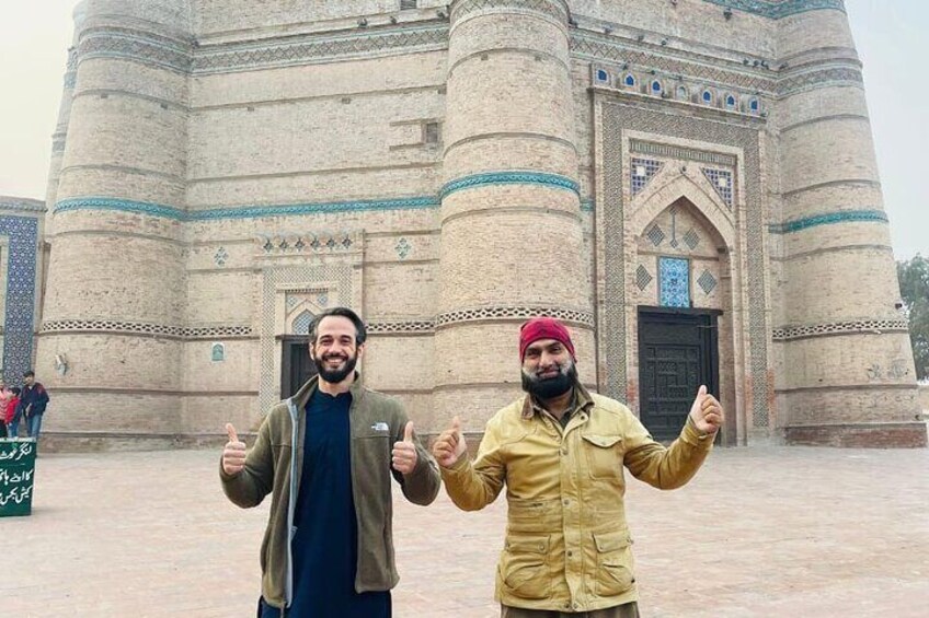 Two men giving thumbs up in front of a large, historic building with intricate architectural details. 2