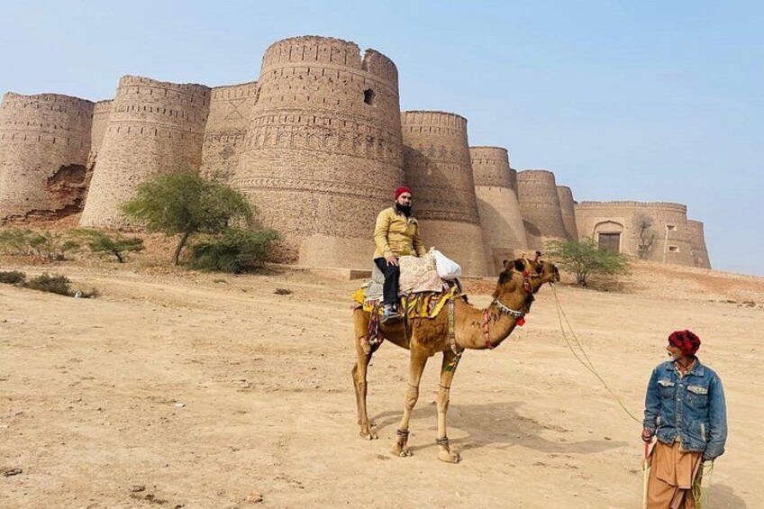 A camel with a rider in a desert landscape with ancient fortifications in the background. 1