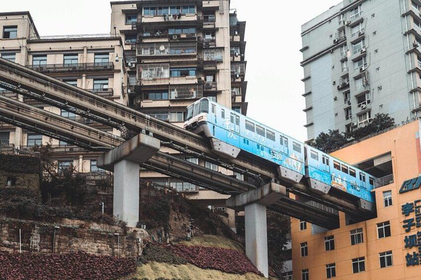 Un train bleu circule sur une voie surélevée, au-dessus d’une colline où se trouvent des bâtiments. 2