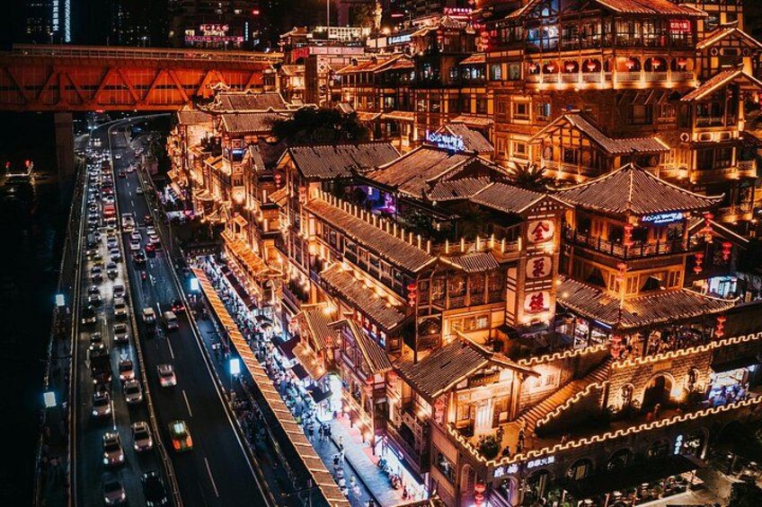 Un ensemble de bâtiments traditionnels, illuminés de façon éclatante, comprenant plusieurs niveaux, avec un pont rouge bien visible en arrière-plan. 5