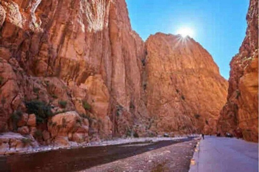 A narrow canyon road flanked by steep red rock cliffs, with a clear sky and sunlight. 4