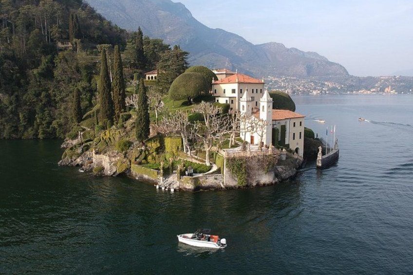 A lake with a small island featuring a white building with a red roof, surrounded by trees and mountains in the background. 1