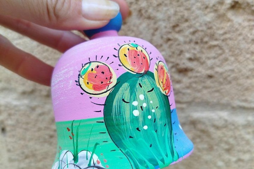 Une main tenant un objet peint orné d’un motif représentant un cactus et une pastèque. 3