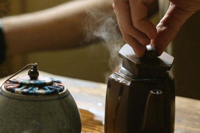A hand adjusting a kettle's lid, steam rising from the pot. 3