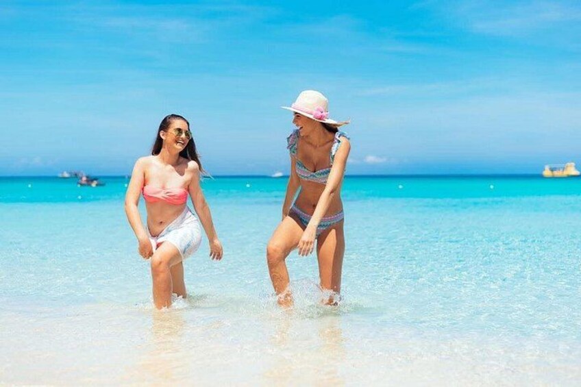 Due persone camminano in acque basse su una spiaggia con acqua blu cristallina e una barca all'orizzonte. 4