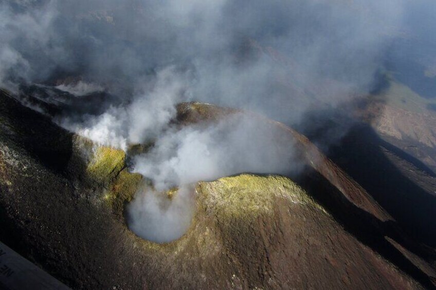 A volcanic crater with steam rising, surrounded by rugged terrain. 4