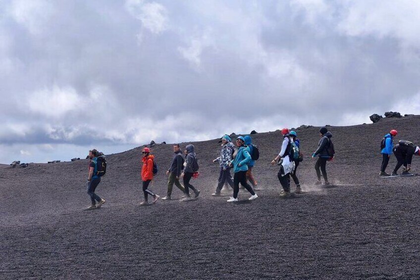 A group of hikers on a volcanic terrain with a cloudy sky. 2