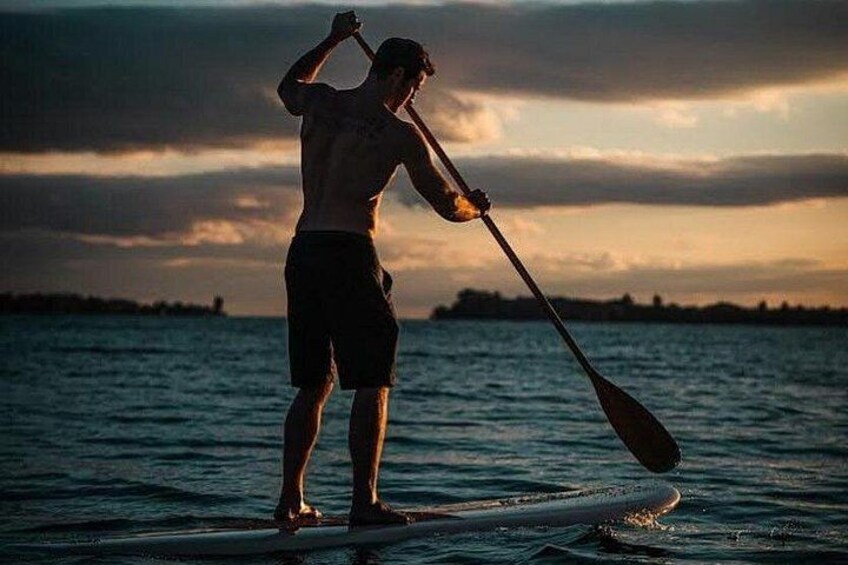 Eine Person steht auf einem Paddleboard auf dem Wasser, während die Sonne untergeht. 4