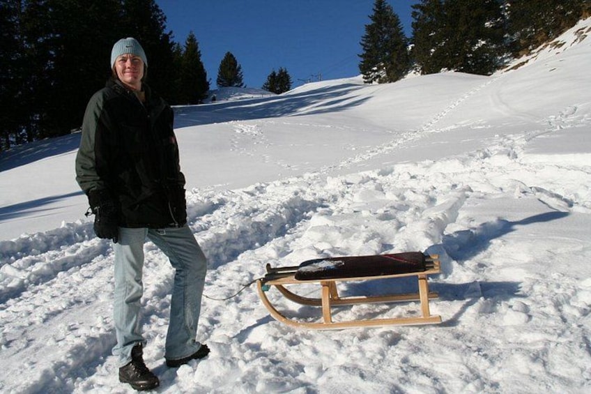 A person standing next to a sled on a snowy slope. 5
