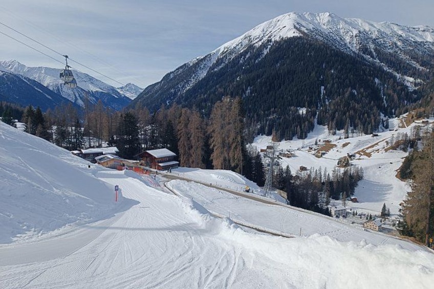A snow-covered ski slope with a ski lift, buildings, and mountains in the background. 4