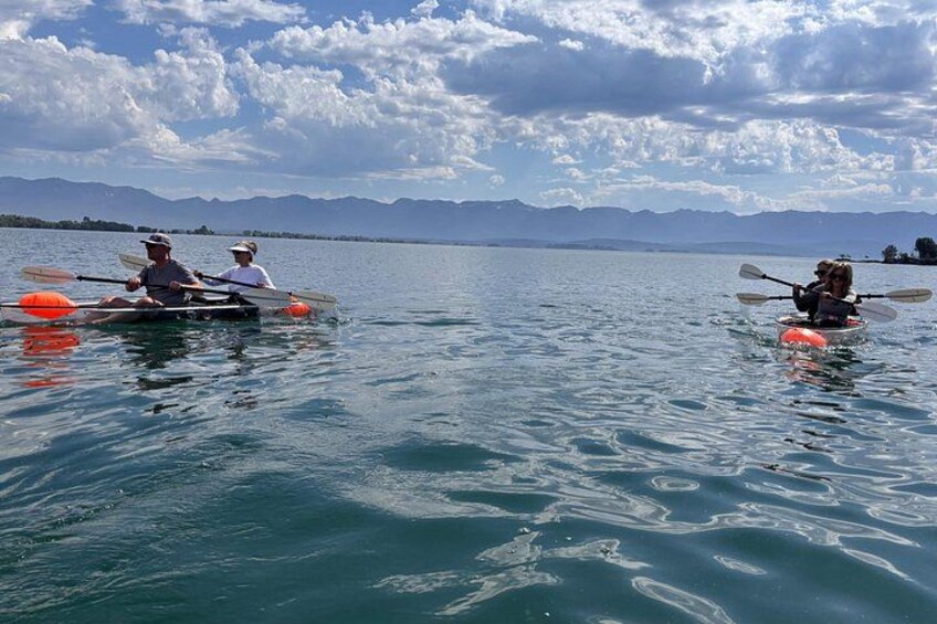 Two people kayaking on a calm lake with mountains in the background. 3