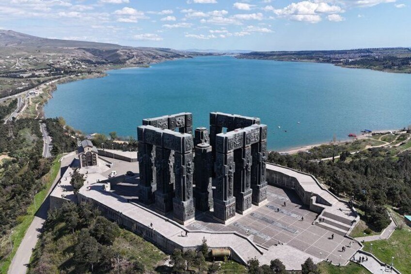 Une vaste structure historique en pierre, entourée d’une zone pavée, qui se détache sur un paysage composé d’une étendue d’eau importante et de collines lointaines. 1