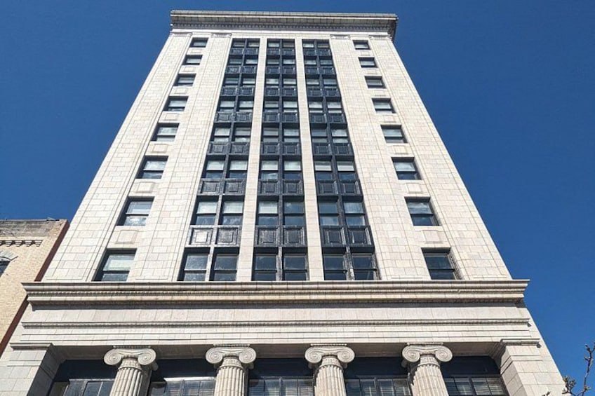 A tall building with a classical architectural style, featuring a series of columns at the base and a grid of windows. 2