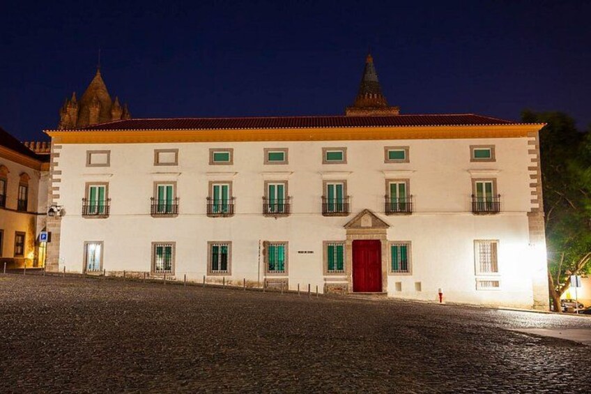 A historic building with a red door and green shutters, a cobblestone street, and a clear night sky. 2