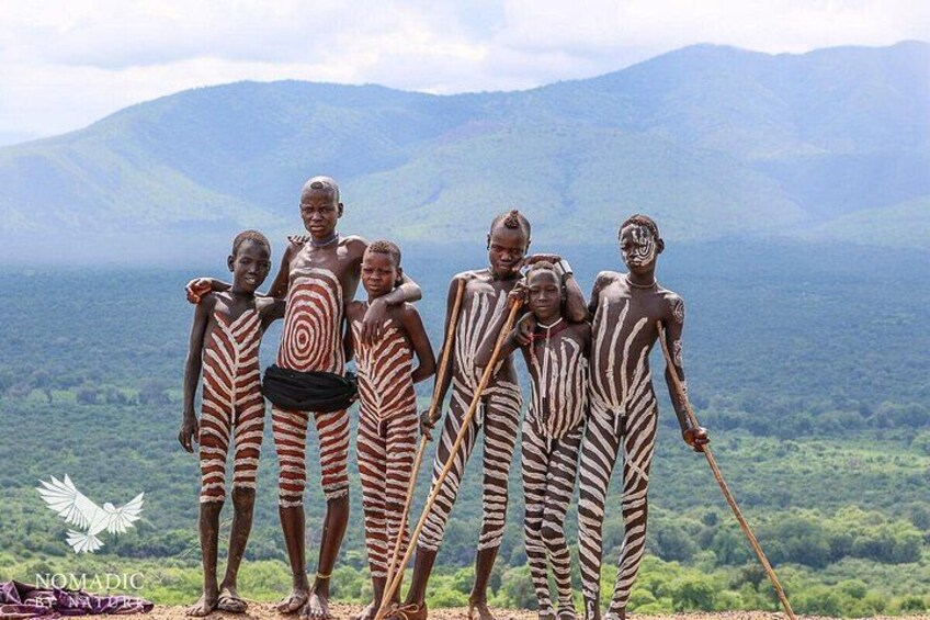 A group of people in patterned attire standing on a hill with a mountainous landscape in the background. 4