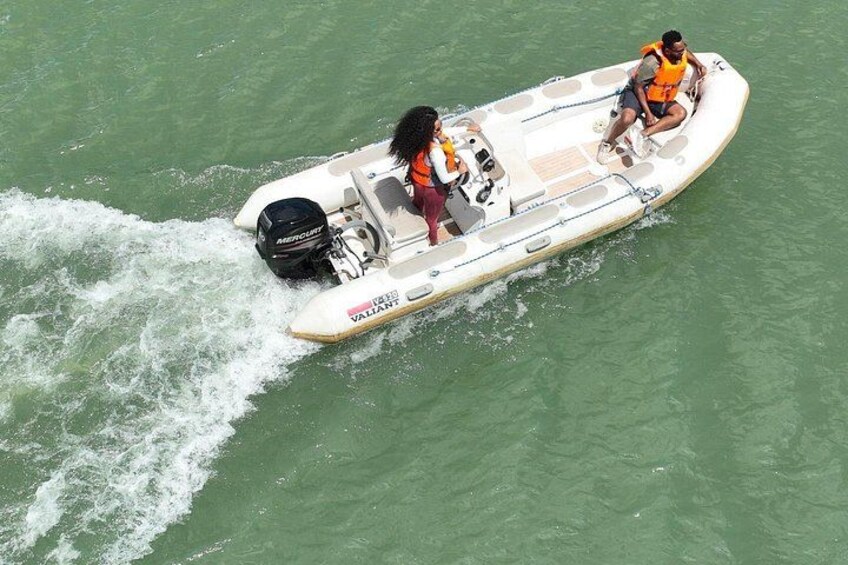 A speedboat with two people wearing life jackets, one in an orange vest and the other in a red vest, moving through greenish water. 3