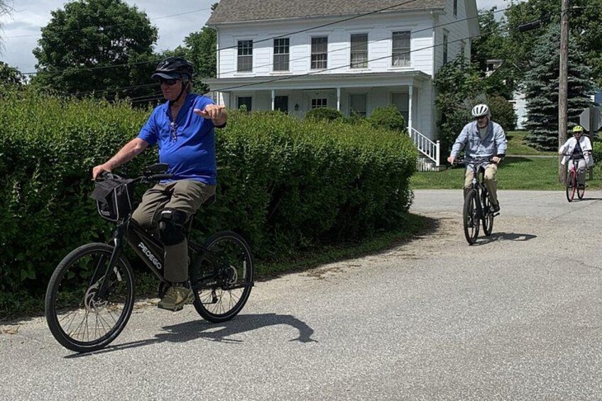 A man riding a bicycle on a gravel path, with a house and greenery in the background. 4