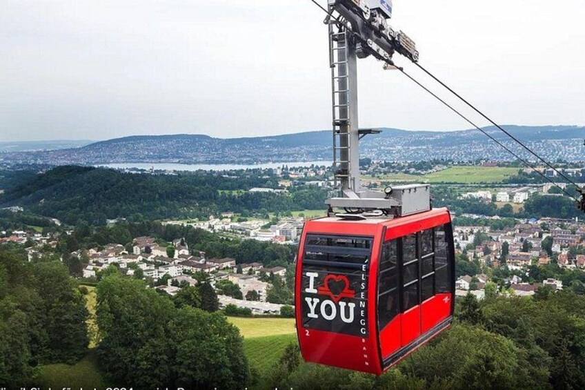 A red cable car with 'I ♥ YOU' written on it, suspended by a cable above a town. 2