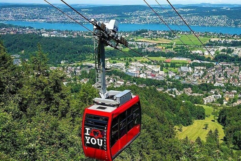 A red cable car with 'I ♥ YOU' text, suspended above a lush green landscape with a city in the background. 5