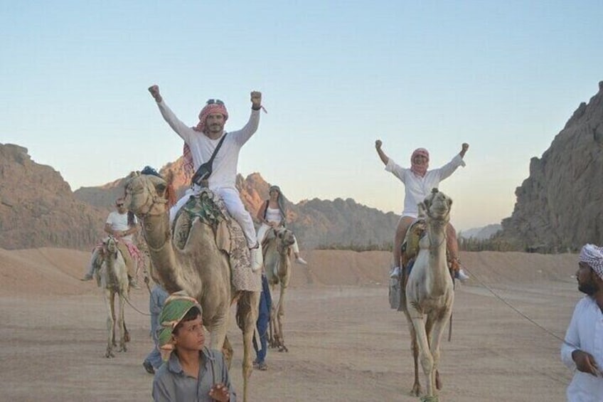 People riding camels in a desert landscape with rocky terrain. 4