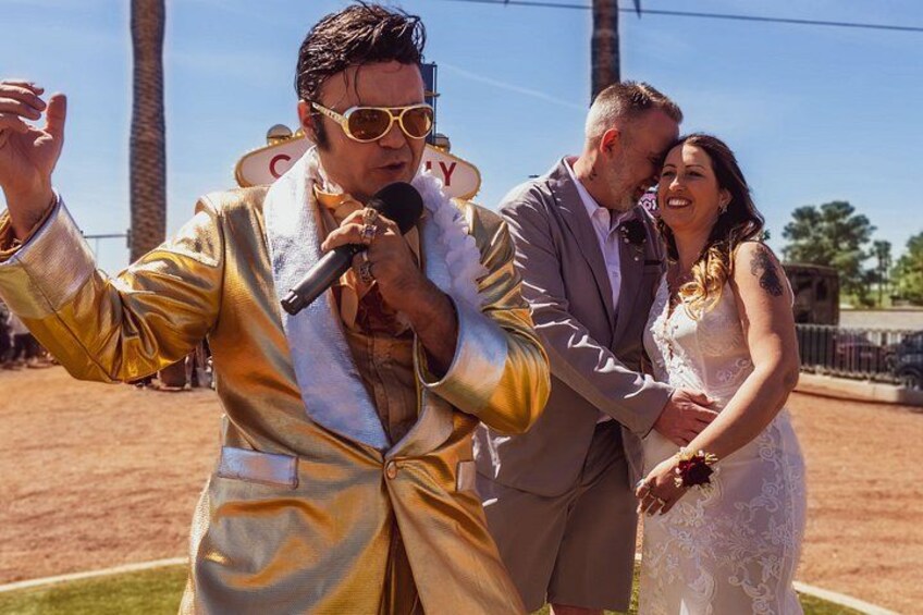 A person in a shiny gold jacket holding a microphone, another in a white dress, and a third in a suit. 4
