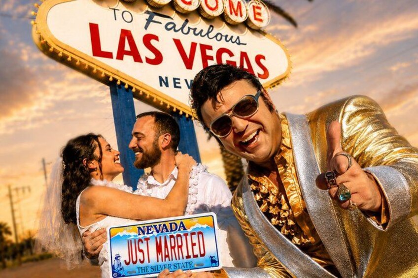 A couple holding a 'Just Married' Nevada license plate sign with a 'Las Vegas' sign in the background. 1