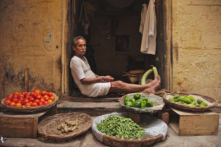 A man sitting outside a shop with baskets of tomatoes, green chilies, and other vegetables. 3