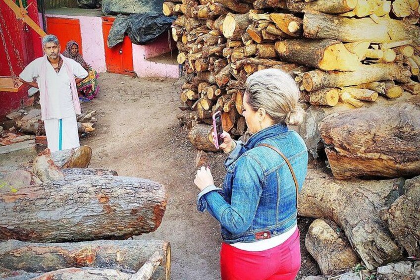 A woman taking a photo, a man standing, and a pile of logs in a rustic outdoor setting. 2