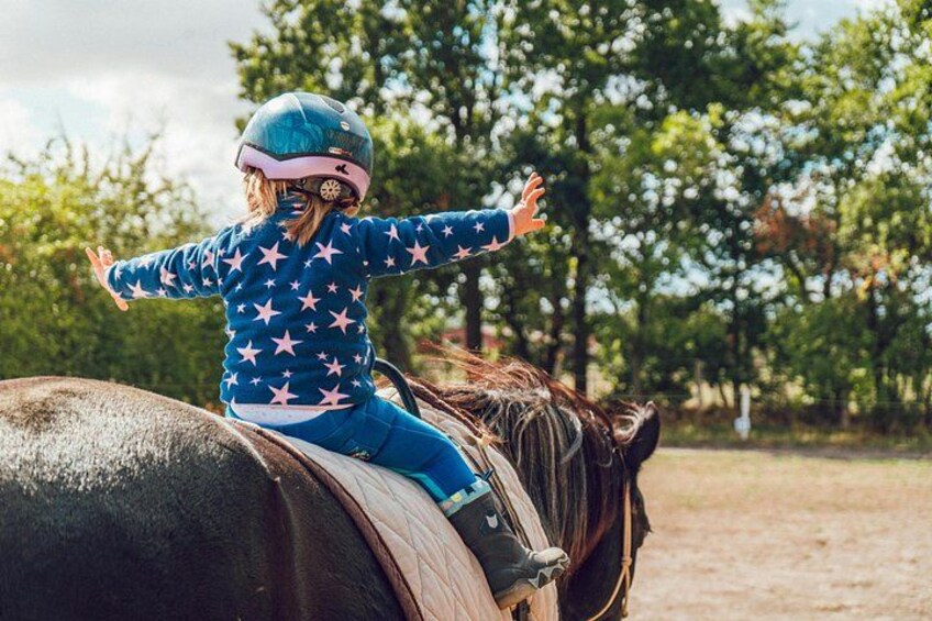 Un niño montando a caballo en un entorno al aire libre, con árboles de fondo. 5