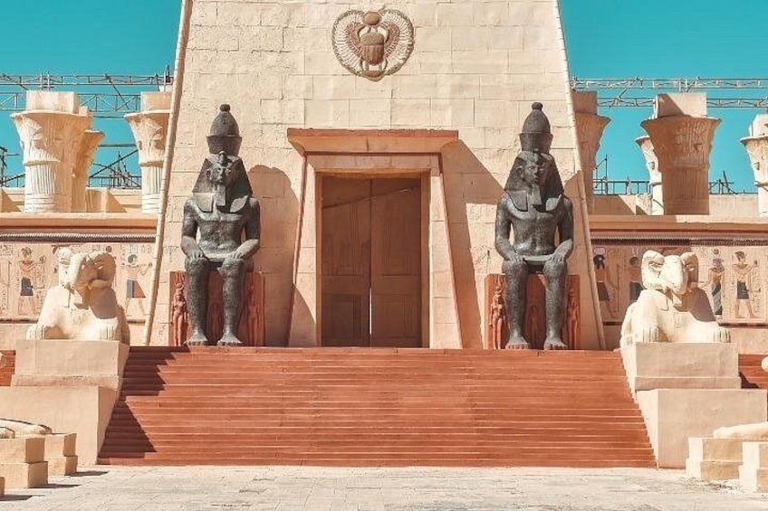 Una entrada imponente con una puerta de madera grande, flanqueada por dos estatuas sentadas y un emblema central. 5