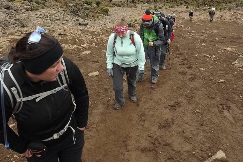 A group of hikers on a dirt trail with rocky terrain and sparse vegetation. 2