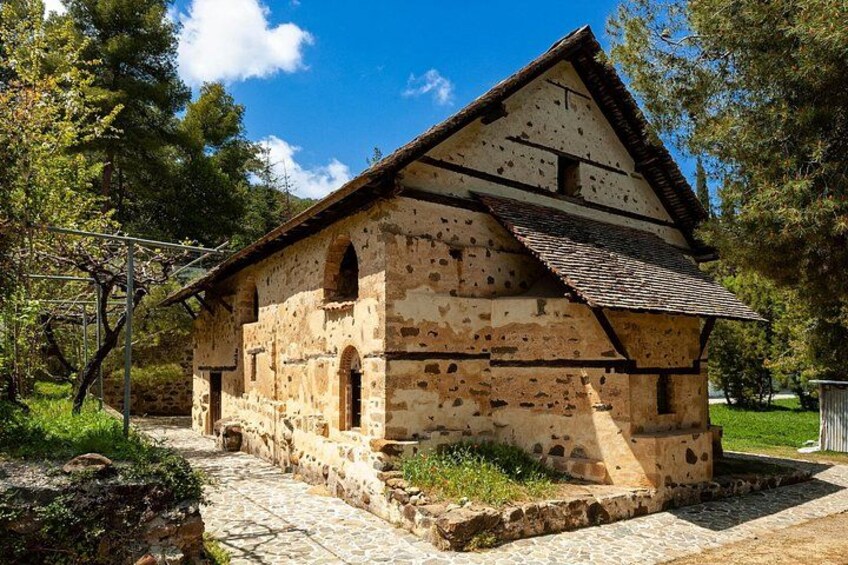 A rustic stone building with a sloped roof, surrounded by trees and a stone pathway. 2