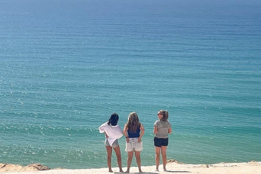 Three people standing on a beach looking at the ocean. 3